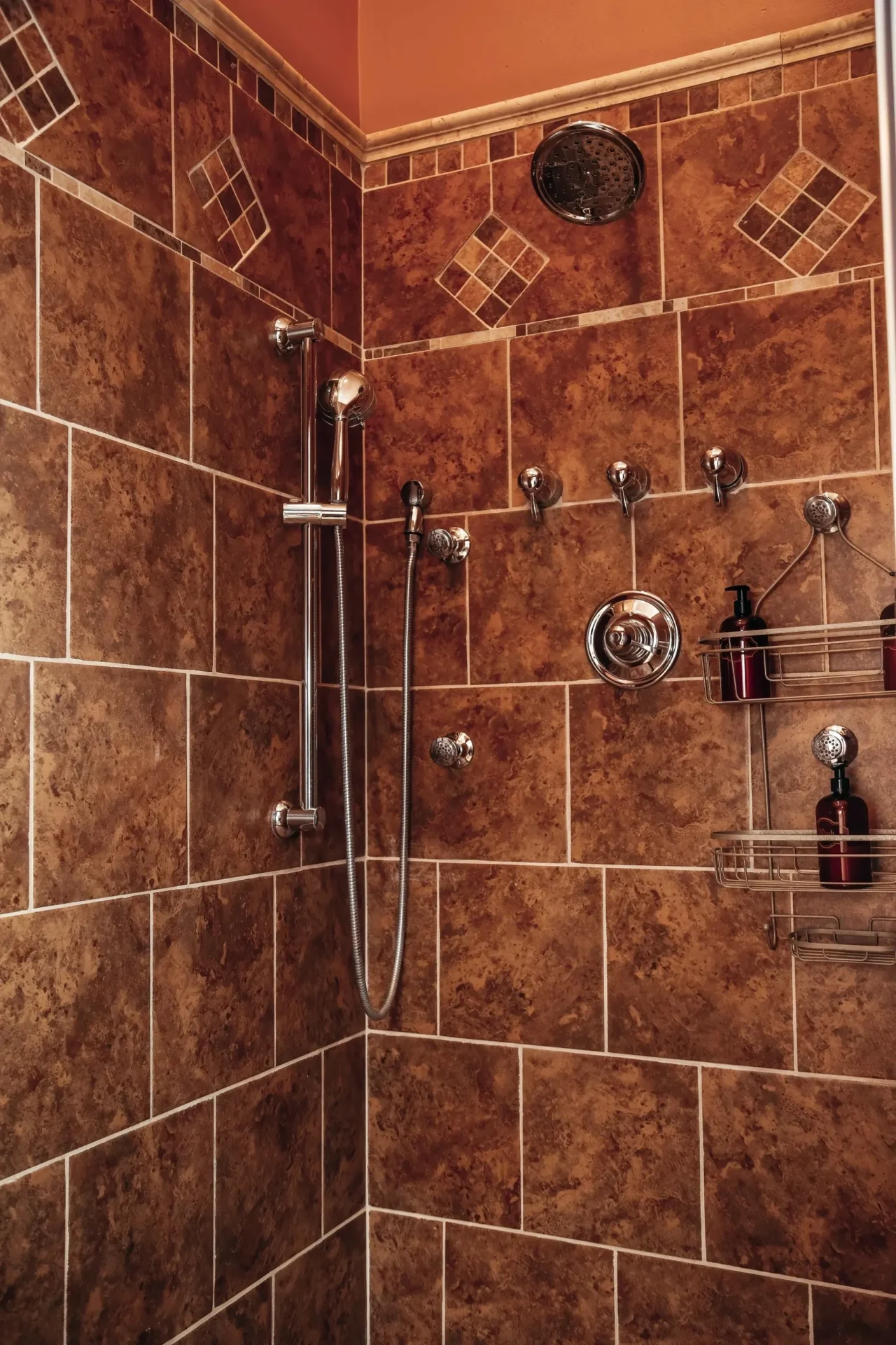 A tiled shower with brown tile and a silver handle.